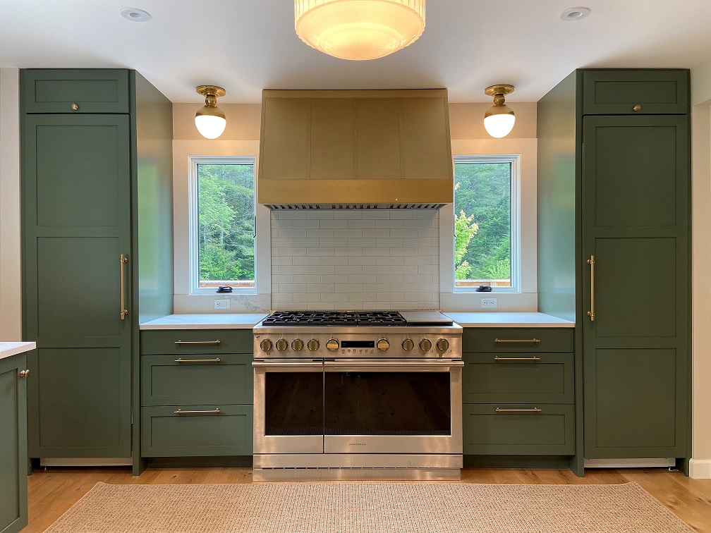 Green kitchen has brass range hood with a gold finish