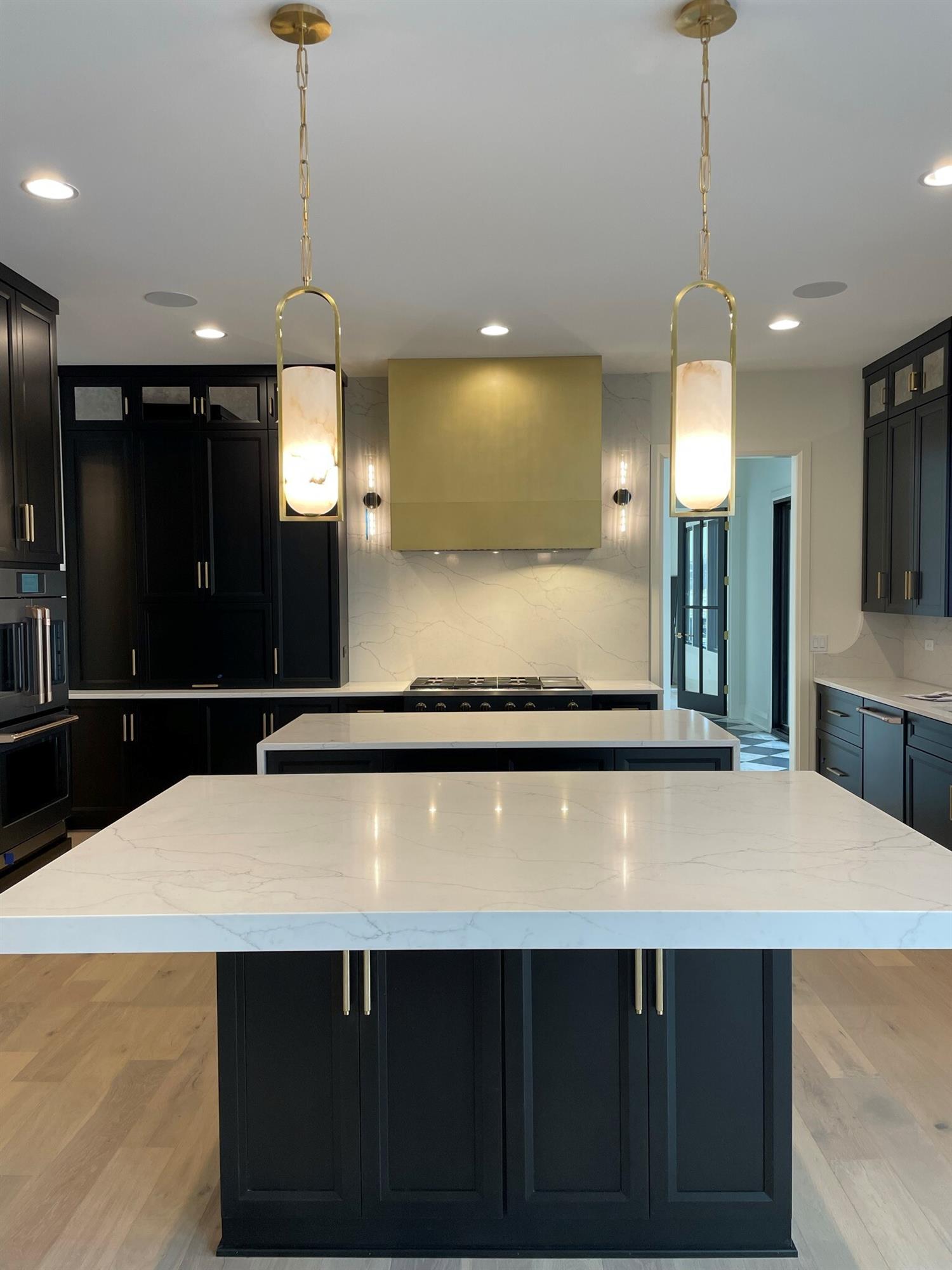 Brass "Minneapolis" range hood in kitchen with black cabinets